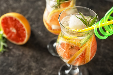 Glass with fresh cold grapefruit cocktail and rosemary on table