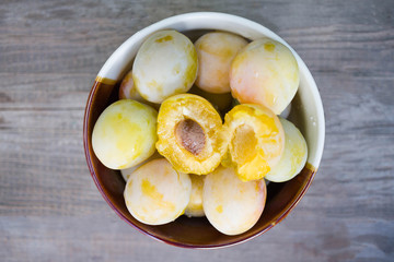 Ripe white plums in a clay bowl on a wooden table. Summer seasonal fruit concept