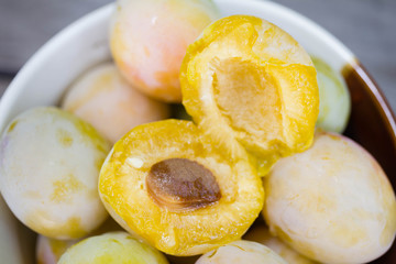 Ripe white plums in a clay bowl on a wooden table. Summer seasonal fruit concept
