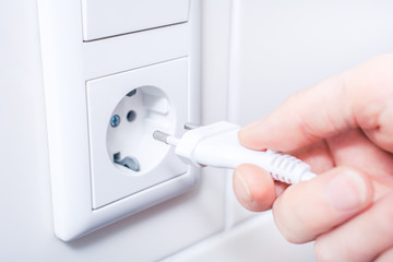 Female Hand Is Holding And Connecting An Electrical Plug In A Wall Socket