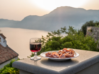 Plate of italian food with cured meat, salami and parmesan cheese and a glass of red wine. Amalfi coast in background.