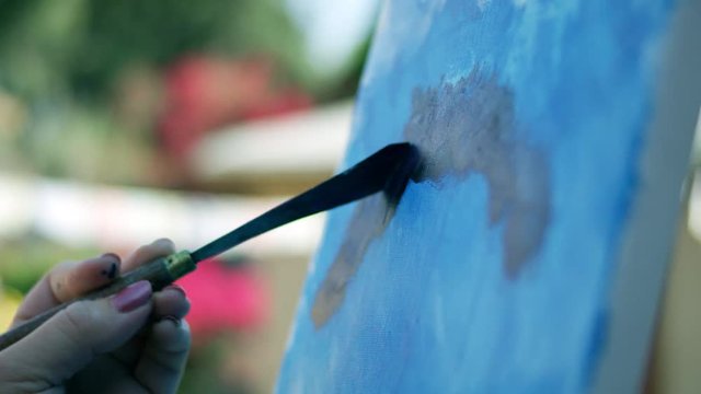 SLOW MOTION video of female artists hand with pink nail varnish applying paint to canvas using knife