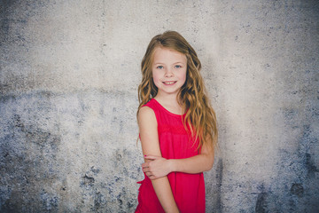 beautiful girl in red shirt in front of concrete background is posing and pointing