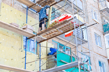 Workers warm and repair the facade of the building. The old house is compacted with mineral wool and the exterior of the building is lined. Work at height without insurance