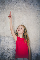 beautiful girl in red shirt in front of concrete background is posing and pointing