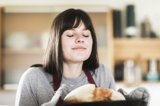 Smiling Woman with her eyes closed standing in the kitchen holding a freshly baked loaf of bread
