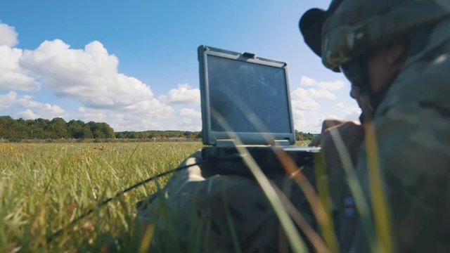 Sliding in and out shot of soldier typing on laptop in field