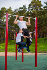 family, father and sons involved in sports on the bar outdoor. Father and sons during street workout in outdoor gym. Strong man and little boys