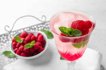Glass of fresh raspberry mojito and bowl with berries on vintage tray