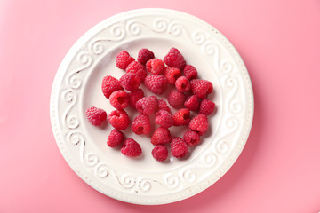 Plate with ripe aromatic raspberries on color background