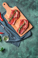 Wooden board with raw meat, rosemary and spices on color textured background