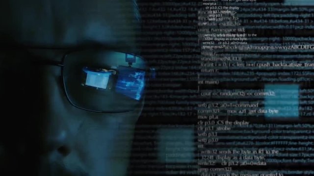 Programmer or hacker in glasses looking on monitor - software code reflecting in the glass and flying around. Caucasian man face in the dark. Digital technologies, software development.