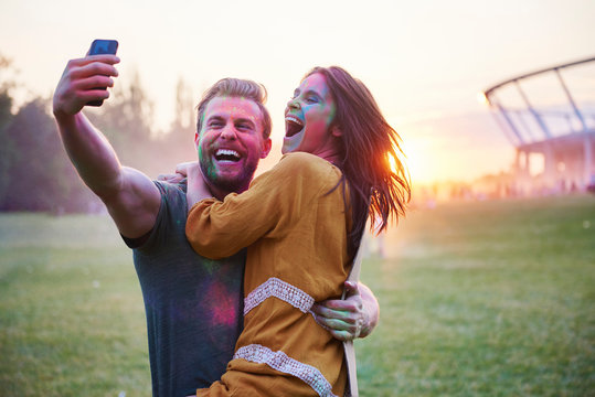 Young couple covered in coloured chalk powder taking selfie at Holi Festival