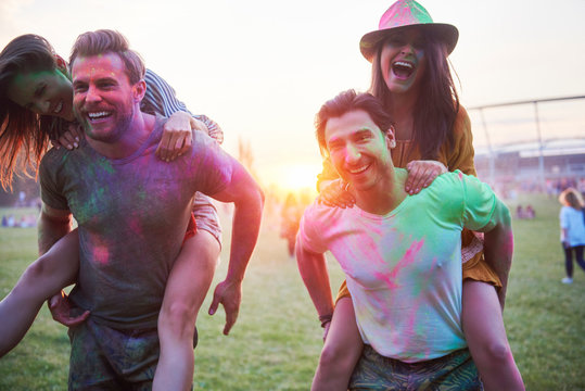 Two young couples covered in coloured chalk powder piggybacking at Holi Festival