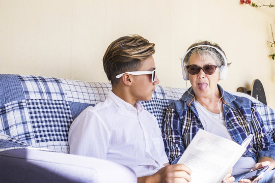 caucasian couple grandmother and grandson study together and listne music or lesson with earphone. the woman do funny crazy expression to the teenager that seriousle go on reading the book