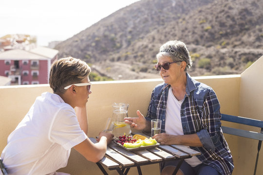 happy leisure activity on the terrace rooftop having breakfast with smiles and happiness for grandmother and teenager family caucasian people. ocean and buildings view, outdoor coule together
