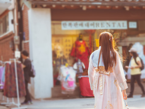 travel and tourist asia concept from beautiful woman in korea traditional cloth (hanbok) relax, take picture in vintage town with soft focus dress rental shop background