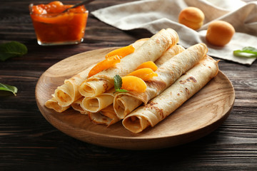 Plate with tasty pancakes and apricots on wooden table