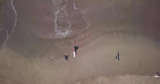Aerial top view waves break on sand beach at sunset. Sea waves on the beautiful beach aerial view drone 4k shot. Bird's eye view of ocean waves and sporty surfers with surfing boards from above.