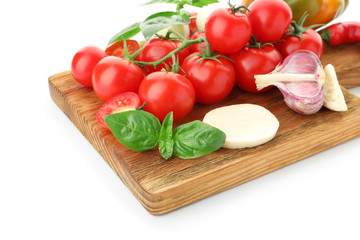 Board with ripe cherry tomatoes, cheese, garlic and herbs on white background