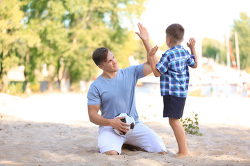 Little boy and his dad with soccer ball giving high five outdoors