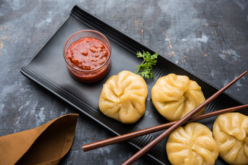 Traditional dumpling momos food from Nepal served with tomato chutney over moody background....