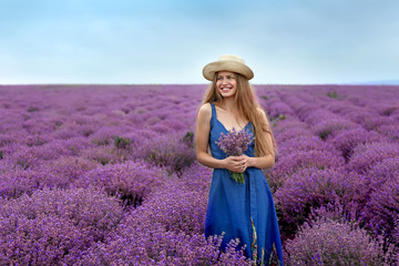 Beautiful young woman with bouquet of lavender in field on summer day