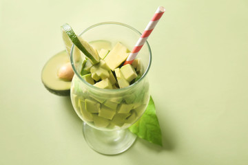 Glass with pieces of ripe avocado on color background
