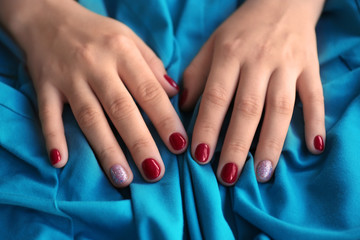 Fototapeta premium Woman's hands with red and glitter nail polish on a blue fabric, beauty and self-care concept, the contrasting colors highlight the detailed nail art and the soft texture of the cloth