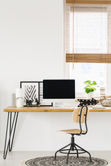 Computer on a wooden desk with metal legs and an industrial swivel chair on a round rug in a...