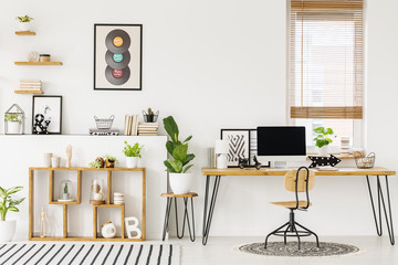 Hipster, white home office interior with natural, wooden furniture, industrial elements, green plants and a computer on a big desk