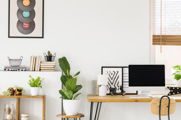 Natural and creative study space interior for a teenager with plants, wooden furniture, computer and a poster on a white wall