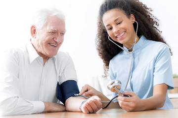 Smiling doctor with stethoscope examining happy elderly man in the hospital