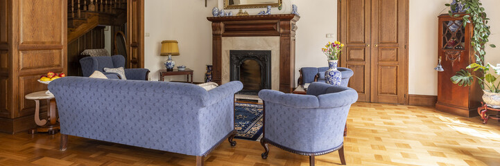 Blue sofa and armchairs classic living room interior with wooden floor and fireplace. Real photo