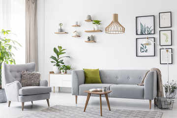 Creative, wooden pendant light above a gray sofa and a comfy armchair in a scandinavian living room...