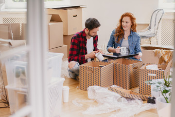 Happy young people packing stuff into boxes while moving out from home