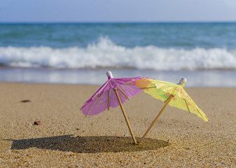 umbrella from a cocktail in female hands on a beach background on a sunny day