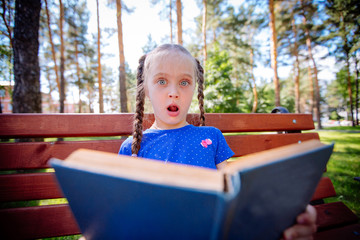 Cute little girl is reading a book outdoors