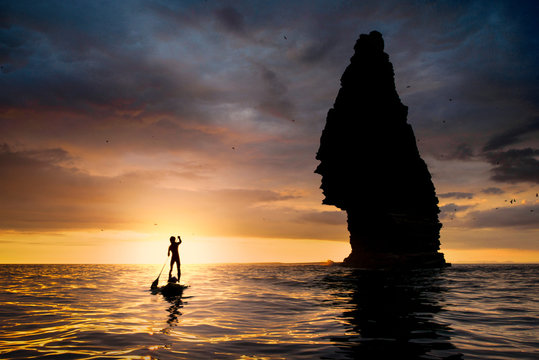 Paddle boarder on water at sunset, beside sea stack, Cliffs of Moher, Doolin, Clare, Ireland