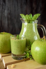 Green smoothie in a glass and in a jug against the wooden background