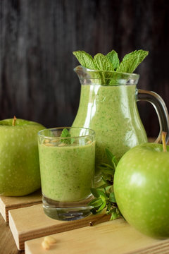 Green smoothie in a glass and in a jug against the wooden background