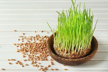 Wooden bowl with sprouted wheat grass and scattered grains on table