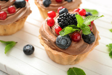 Tasty tartlets with chocolate cream and berries on white board, closeup