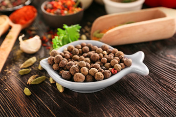 Bowl with allspice on wooden table