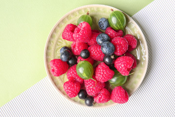 Plate with delicious ripe berries on color background