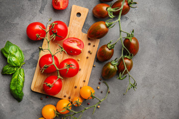 Wooden board and fresh cherry tomatoes of different sorts on grey background