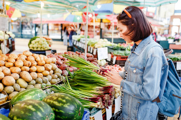 Happy young brunette choosing and picking some vegetables at the grocery market