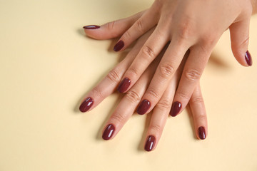 Hands of woman with stylish dark red manicure on color background