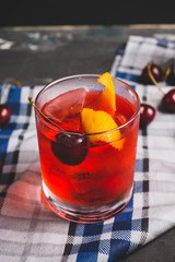 Old fashioned cocktail with cherry and orange peel. Selective focus.