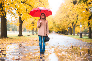 Happy woman with red umbrella walking at the rain in beautiful autumn park.